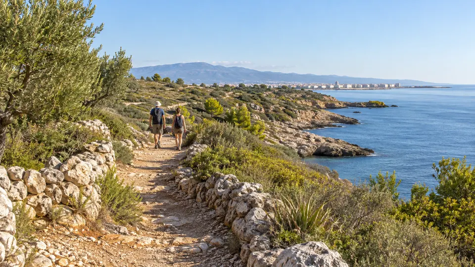 Ilustración generada con IA de dos personas caminando por una senda mediterránea imaginaria