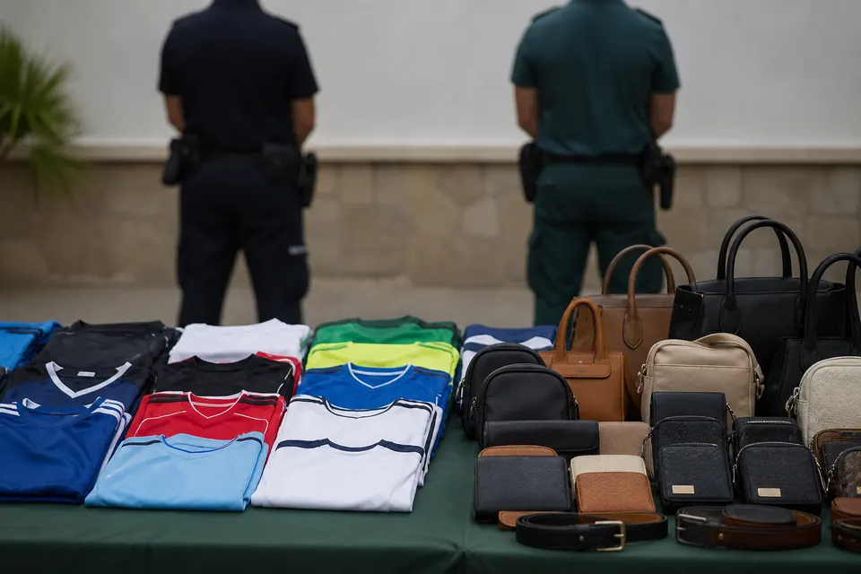 Recreación generada con IA de camisetas y bolsos sin marca dispuestos ante dos agentes genéricos