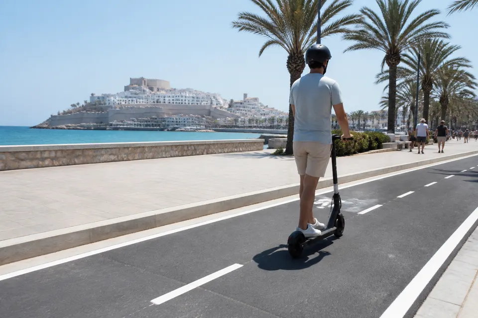 Recreación generada con IA de un usuario de patinete circulando por un carril bici junto al paseo marítimo de Peñíscola